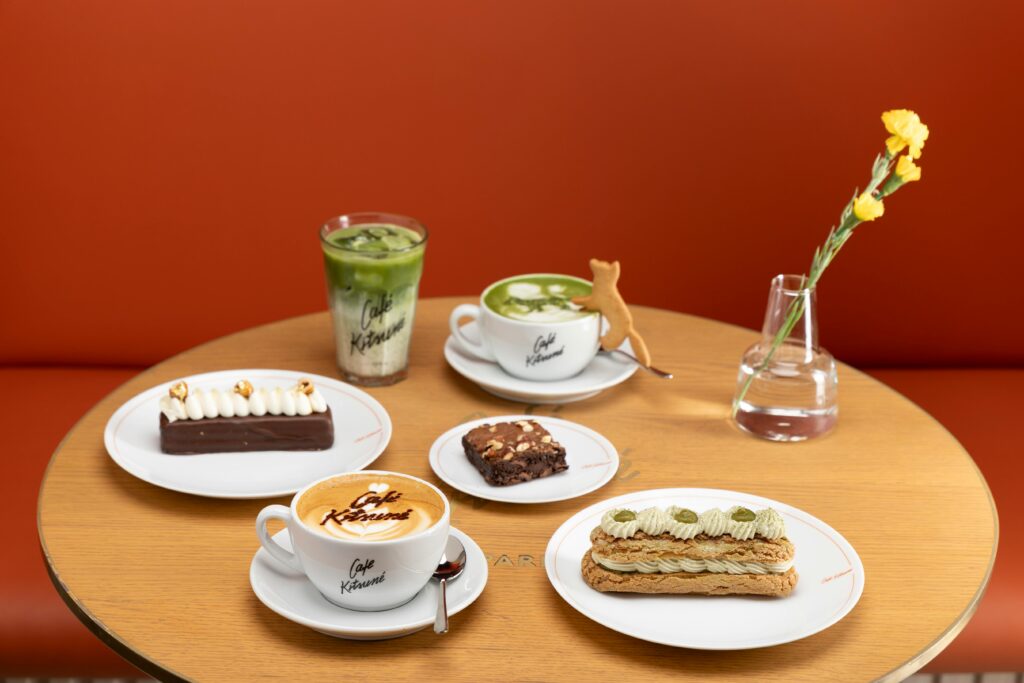 A stylish café table featuring a variety of desserts, drinks, and a flower vase.